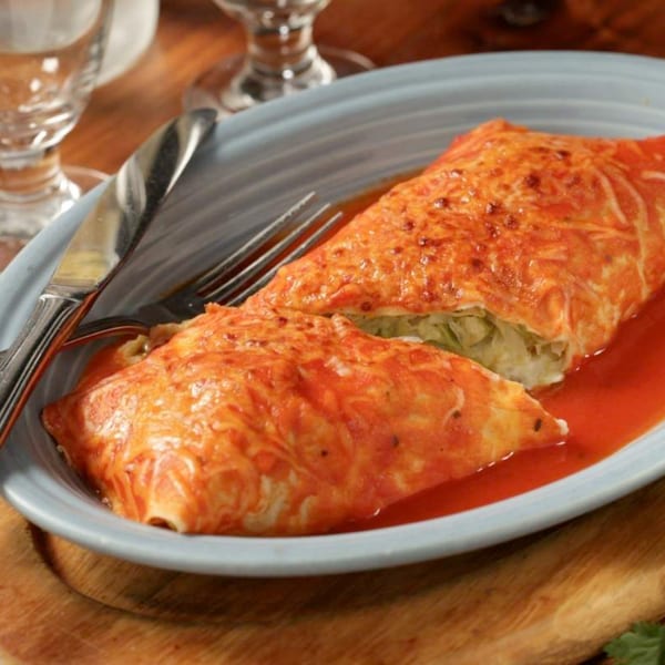 Two cheesy enchiladas covered in red sauce on a light blue plate with silverware.