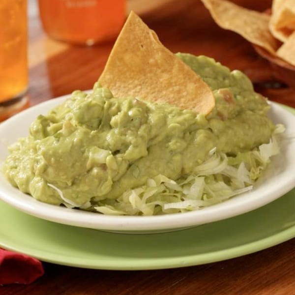 Fresh guacamole with a tortilla chip on a bed of shredded lettuce, served at Tortuga's Mexican Village.