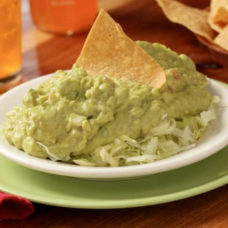 Fresh guacamole with a tortilla chip on a bed of shredded lettuce, served at Tortuga's Mexican Village.