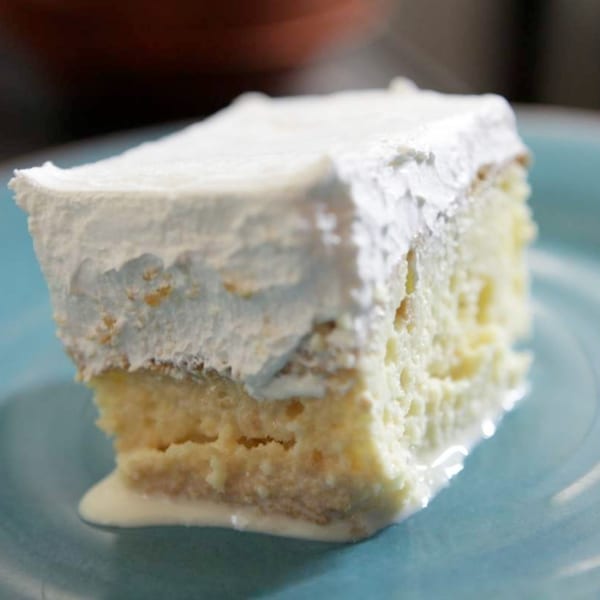 A slice of Tres Leches cake with white frosting and milk pooling on a blue plate.