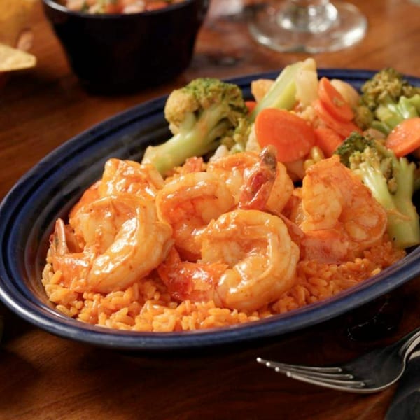 Shrimp with red sauce, rice, and mixed vegetables including broccoli and carrots in a blue dish.
