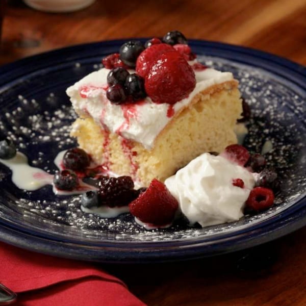 Tres Leches cake with whipped cream, strawberries, blueberries, and raspberries on a blue plate.