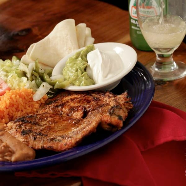 Grilled chicken fajita with rice, beans, guacamole, sour cream, tortillas, and a drink.